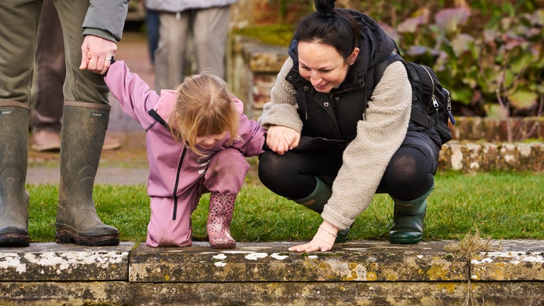 Adult and child bent down looking into a pond